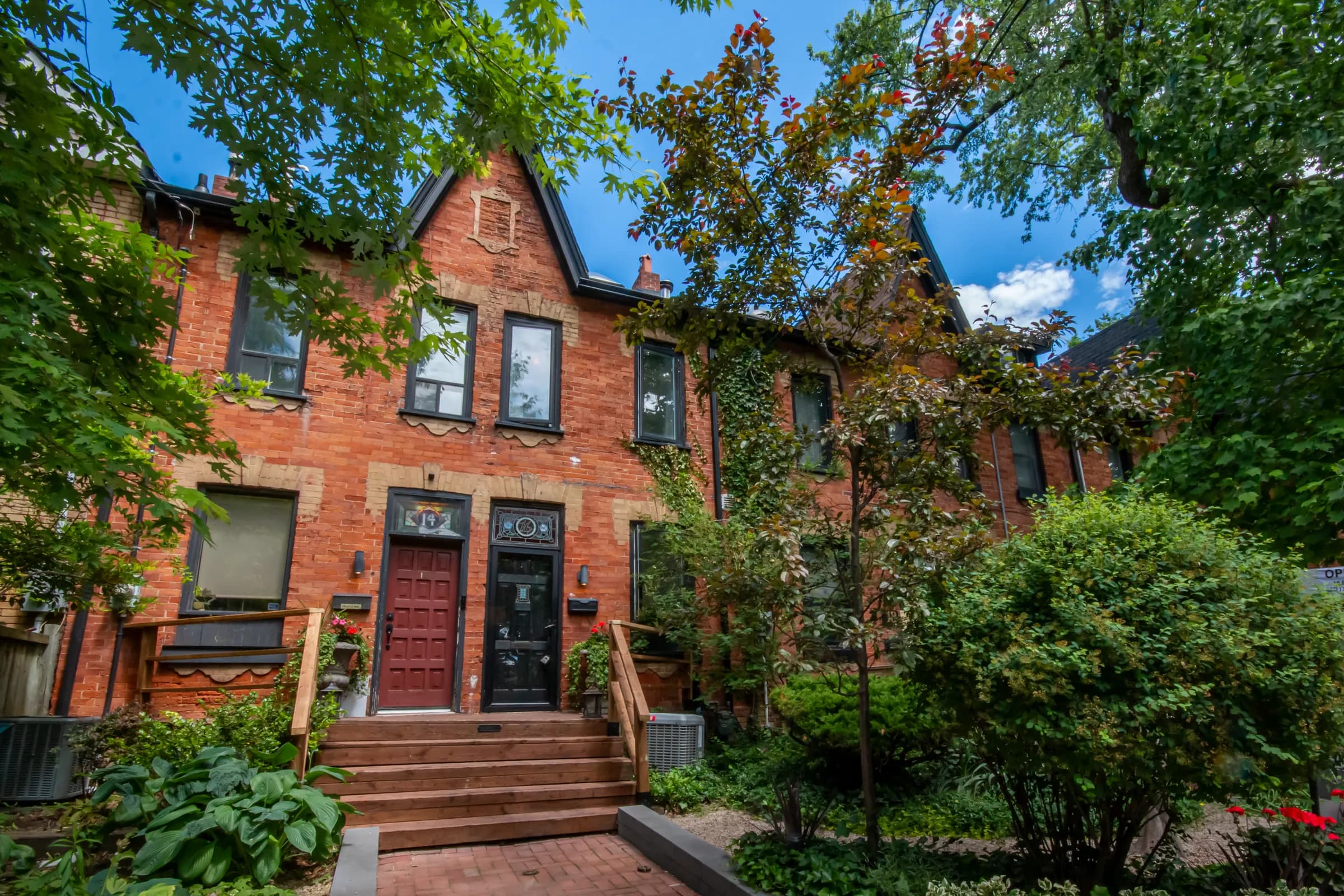 Heritage red-brick Victorian townhome with a gabled roof and mature trees