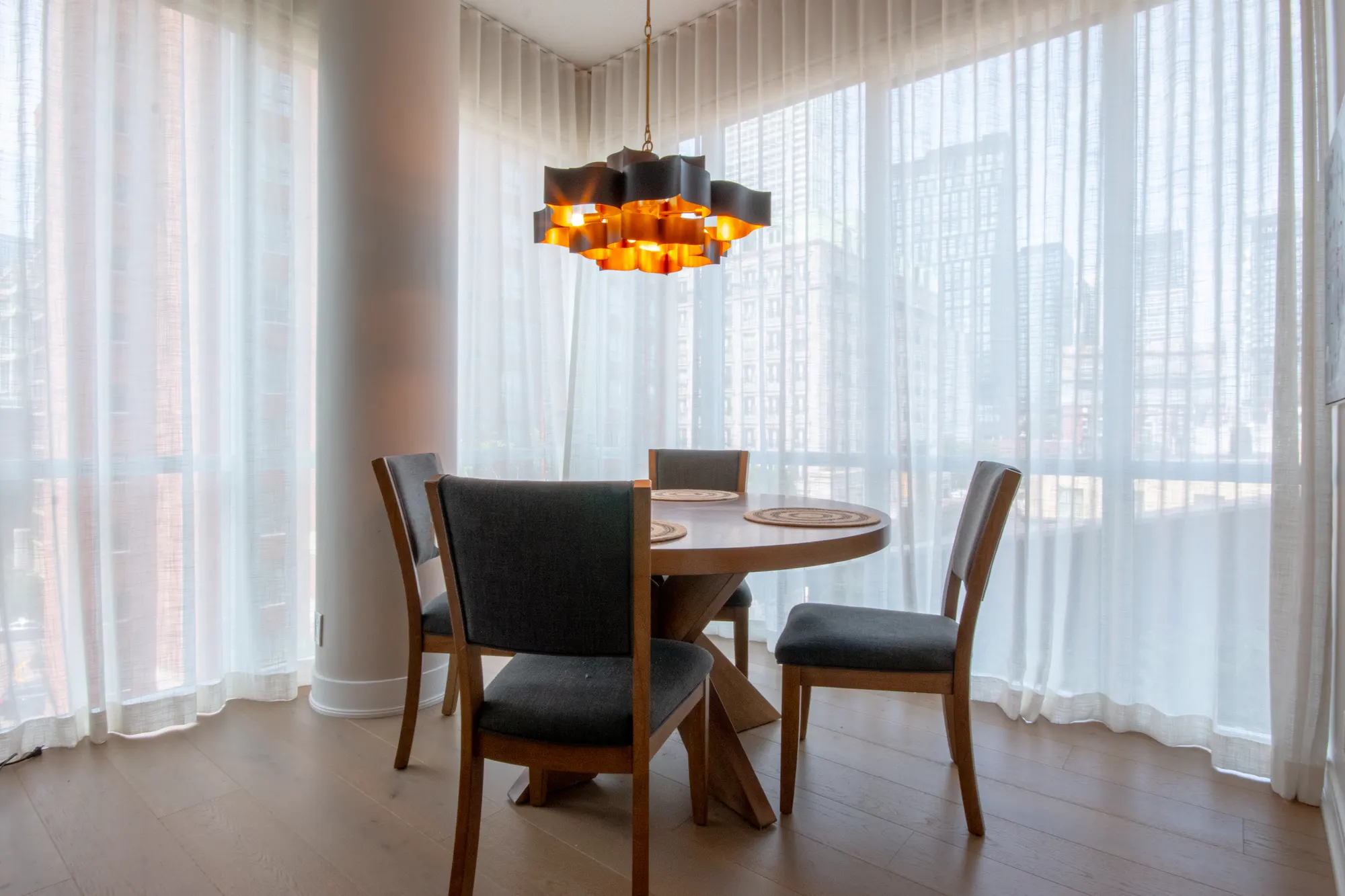 Dining nook wrapped in sheer curtains with a sculptural chandelier and skyline beyond